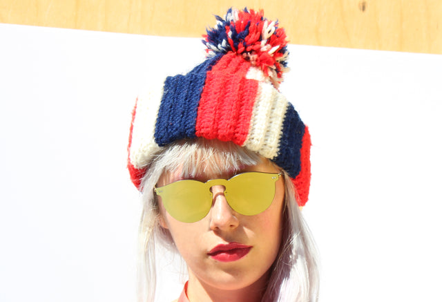 Platinum blond model wearing a red, white, and blue chunky beanie and the Leonard Mask Sunglasses in Gold