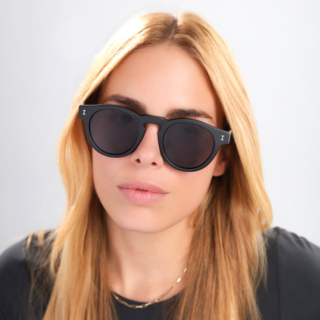 Blond woman in a black tee wearing Leonard Sunglasses Matte Black with Grey