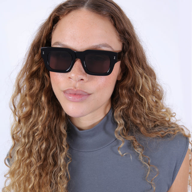Brunette model with wavy hair in a gray mockneck shirt wearing Lewis 50 Sunglasses Black with Grey Flat