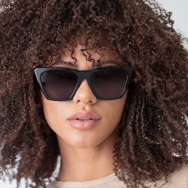 Brunette model with afro-curly hair wearing Lisbon Sunglasses Black with Grey