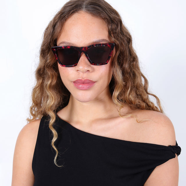 Brunette model with ombré, natural curls wearing Lisbon Sunglasses Hibiscus with Grey