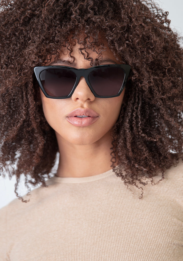 Brunette model with natural, tight curls wearing Lisbon Sunglasses in Black