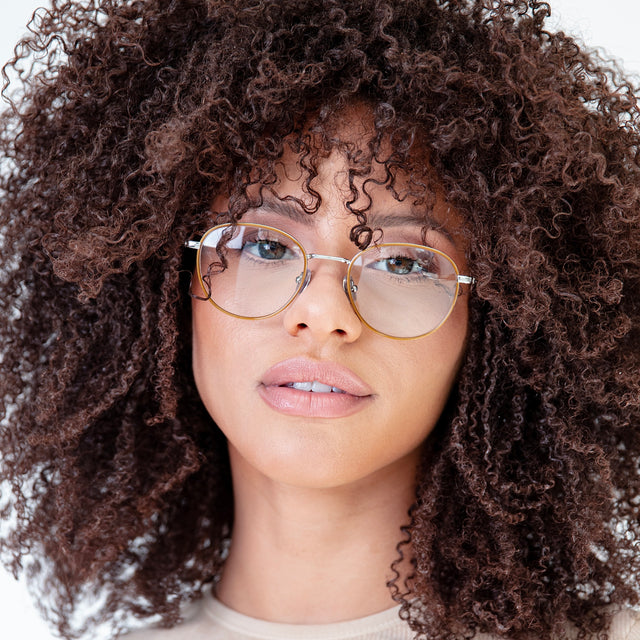 Brunette model with small, tight curls wearing London Optical Saddle/Silver with Optical