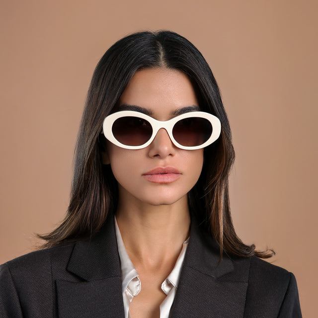 Brunette model in a black wool blazer glancing to her left wearing Luna Sunglasses Cream with Brown Flat Gradient