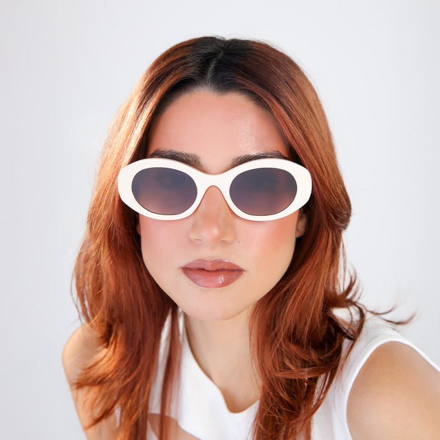 Women with red hair in a white blouse wearing Luna Sunglasses Cream with Brown Flat Gradient