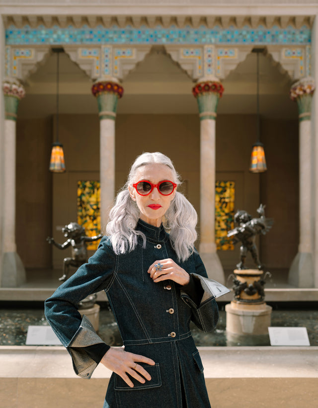 Model with silver hair wearing the Met x illesteva Sunglasses in Red in front of statues at the Met Museum