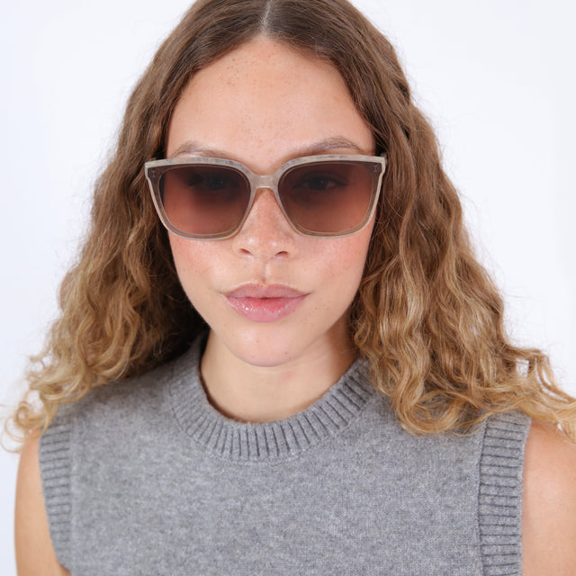 Brunette model with ombre wavy hair in a gray sweater vest wearing Mallorca Sunglasses Bone with Brown Flat Gradient