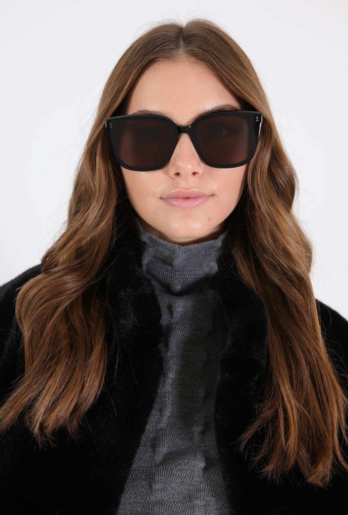 Brunette model in Mallorca Sunglasses in Black paired with a grey turtleneck and black jacket.