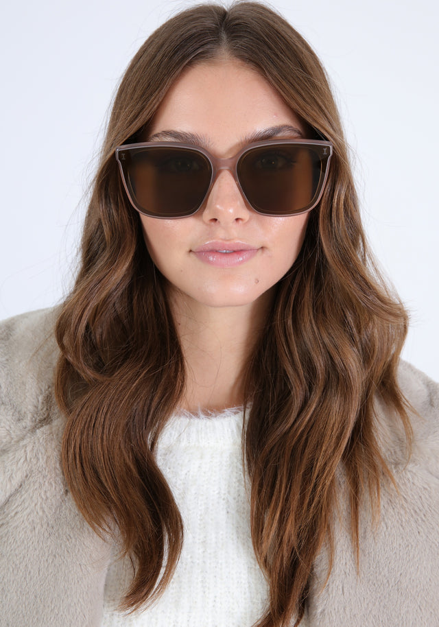 Brunette model with loose curls in a gray, fuzzy jacket wearing Mallorca Sunglasses in Thistle