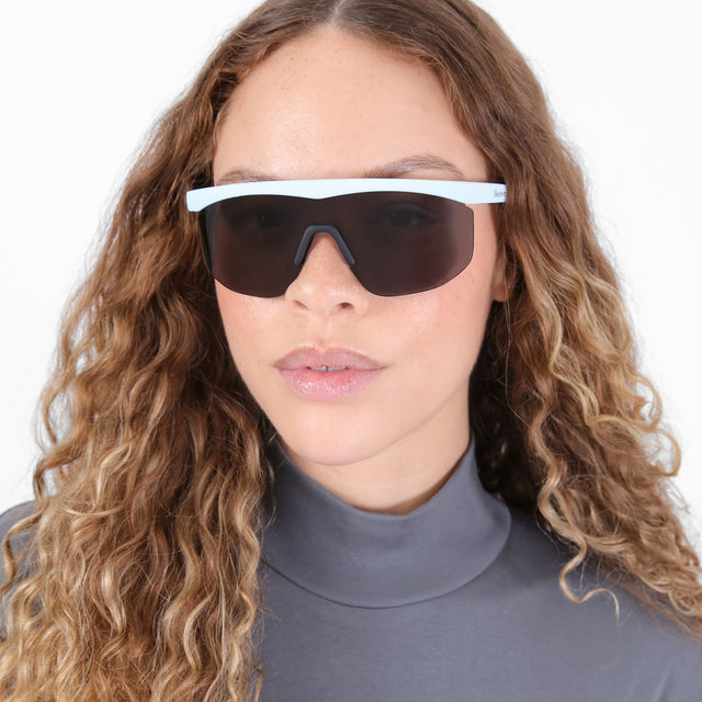 Brunette model with ombré, natural curls wearing Managua Sunglasses Matte Baby Blue with Grey