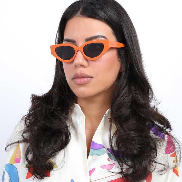 Brunette model with loose curls wearing Mary Lou Sunglasses Aperol with Grey Flat