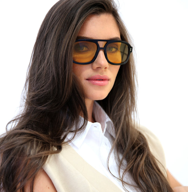 Angled pose of brunette model with wavy hair wearing Memphis Sunglasses Black with Honey See Through