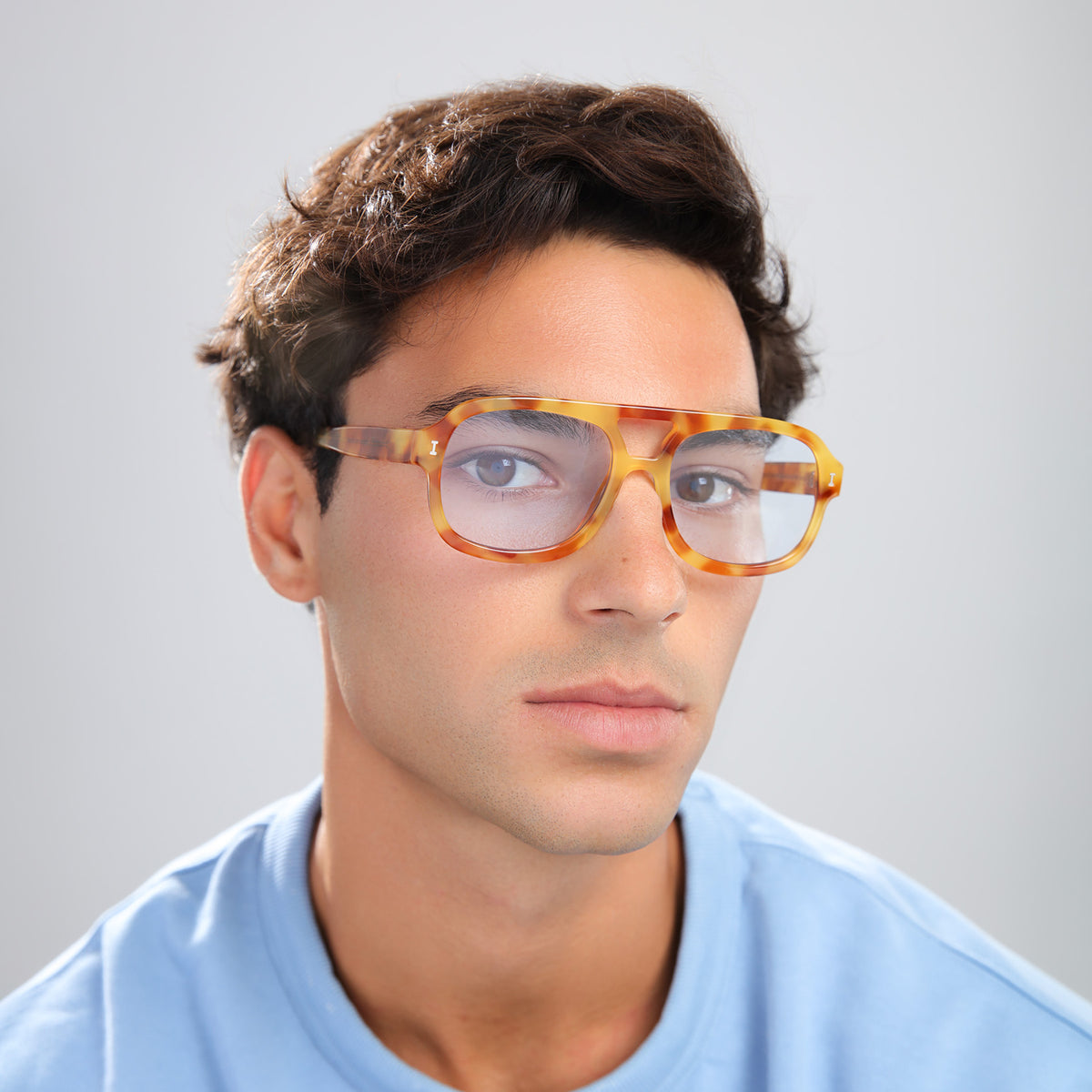 Man wearing Memphis Sunglasses in Amber with Light Blue See Through lenses, side profile, Man in a light blue tee