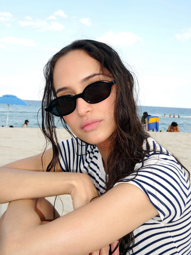 Brunette model at the beach wearing the Munich Sunglasses in Black with Grey lenses