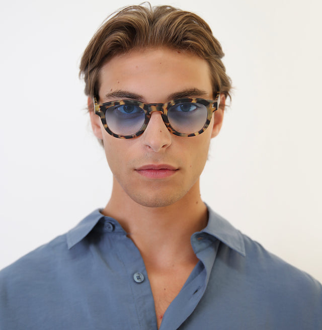 Model with brown hair pushed back wearing Murdoch Sunglasses Matte Tortoise with Blue Gradient See Through