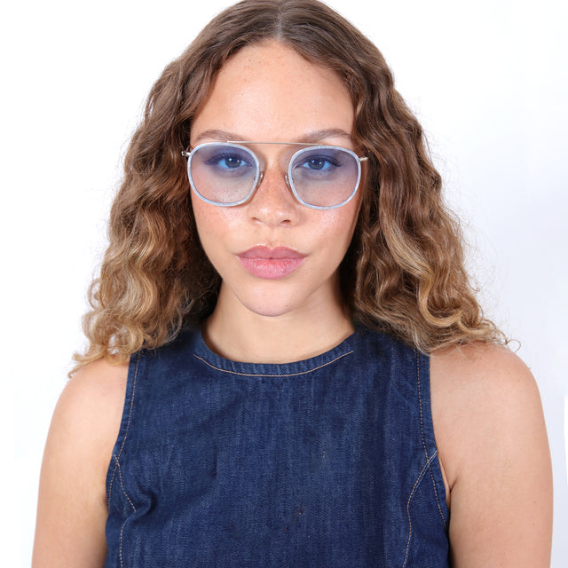Brunette model with ombré, curled hair in a denim high neck blouse wearing Mykonos Ace Sunglasses Celeste/Gold with Blue Flat Gradient See Through