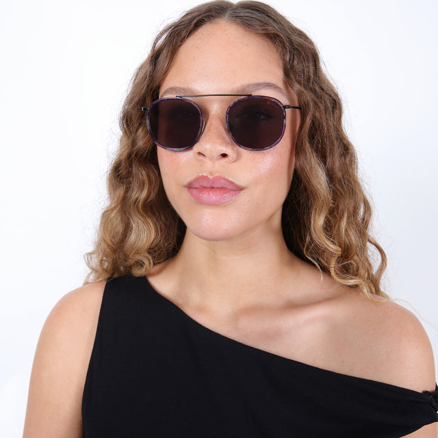 Brunette model with ombré, curled hair wearing Mykonos Ace Sunglasses Iris/Black with Grey Flat