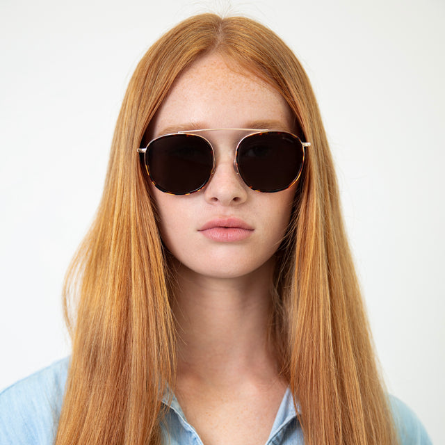Model with straight red hair wearing Mykonos Ace Sunglasses Pecan/Gold with Grey Flat