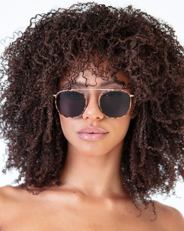 Brunette model with afro-curly hair wearing Mykonos Ace Sunglasses Star Tortoise/Rose Gold with Grey Flat