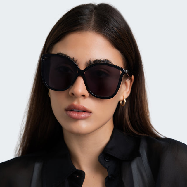 Close up of a woman in a black sheer blouse wearing Nancy 57 Sunglasses Black with Grey