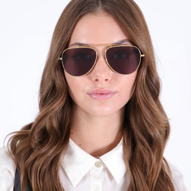 Brunette model with curled hair in a white collared blouse wearing Naxos 58 Sunglasses Gold with Grey Flat
