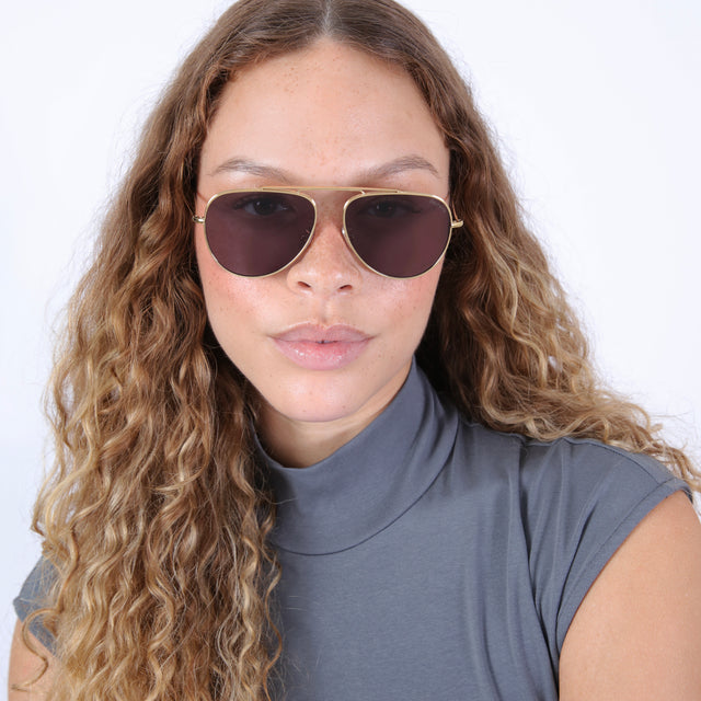 Brunette model with wavy hair in a gray mockneck wearing Naxos 58 Sunglasses Gold with Grey Flat