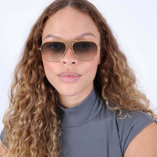 Brunette model with wavy hair in a gray mockneck wearing Naxos 58 Sunglasses Gold with Olive Flat Gradient