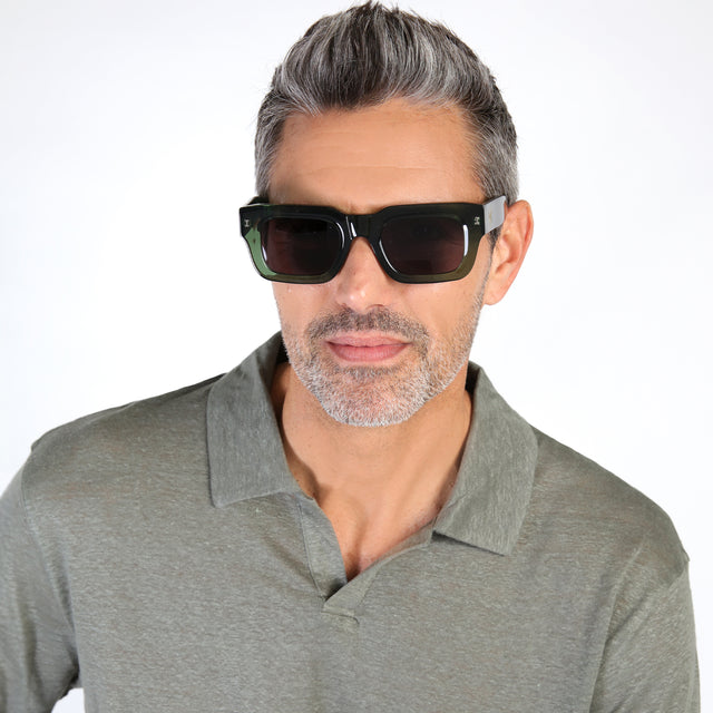 Model with salt and pepper hair and beard wearing Nick Kyrgios x illesteva 2 Sunglasses Pine with Grey Flat