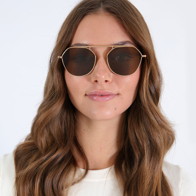 Brunette model with loose curls wearing Nicosia 57 Sunglasses Rose Gold with Brown Flat