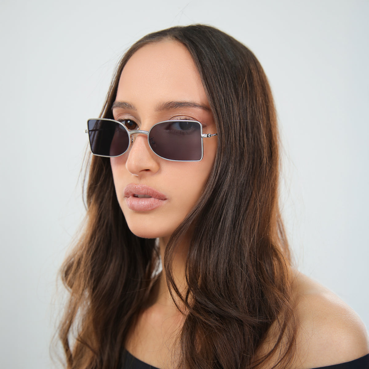 Woman wearing Nostrand Sunglasses in Silver with Grey lenses, side profile, Another angle of woman in an off-the-shoulder blouse