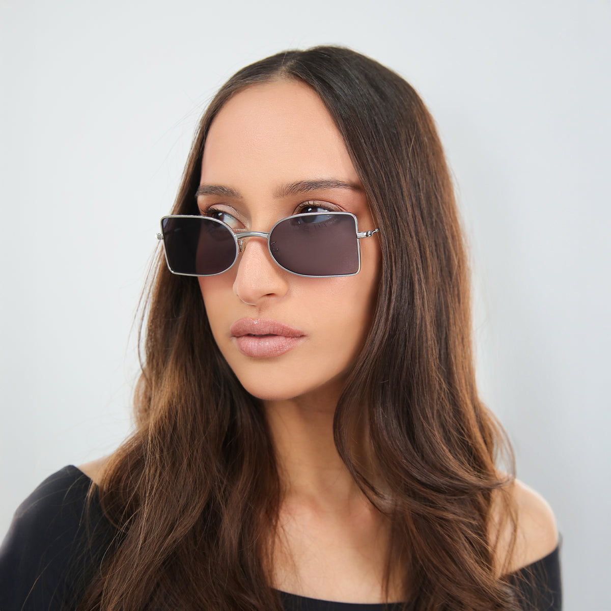 Woman wearing Nostrand Sunglasses in Silver with Grey lenses, side profile, Woman with brown hair in an off-the-shoulder blouse