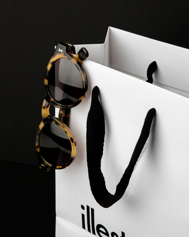 Illesteva Leonard sunglasses elegantly displayed on a shopping bag