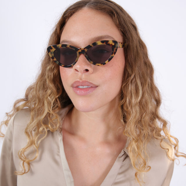 Brunette model with ombre wavy hair in a silk blouse wearing Pamela Sunglasses Tortoise with Grey Flat