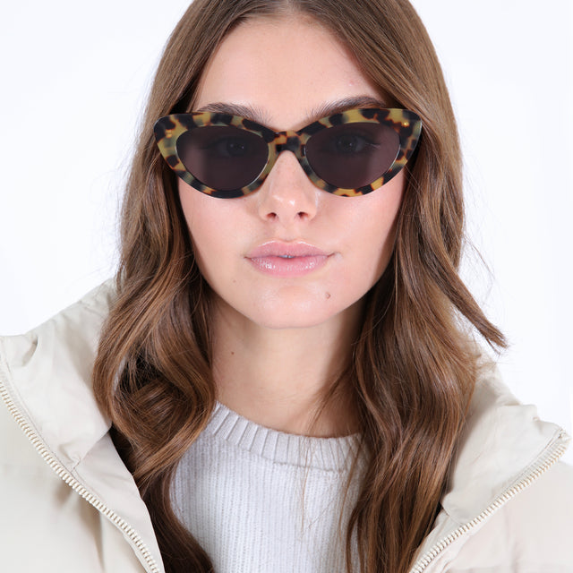 Brunette model with curled hair in a white puffer wearing Pamela Sunglasses Tortoise with Grey Flat