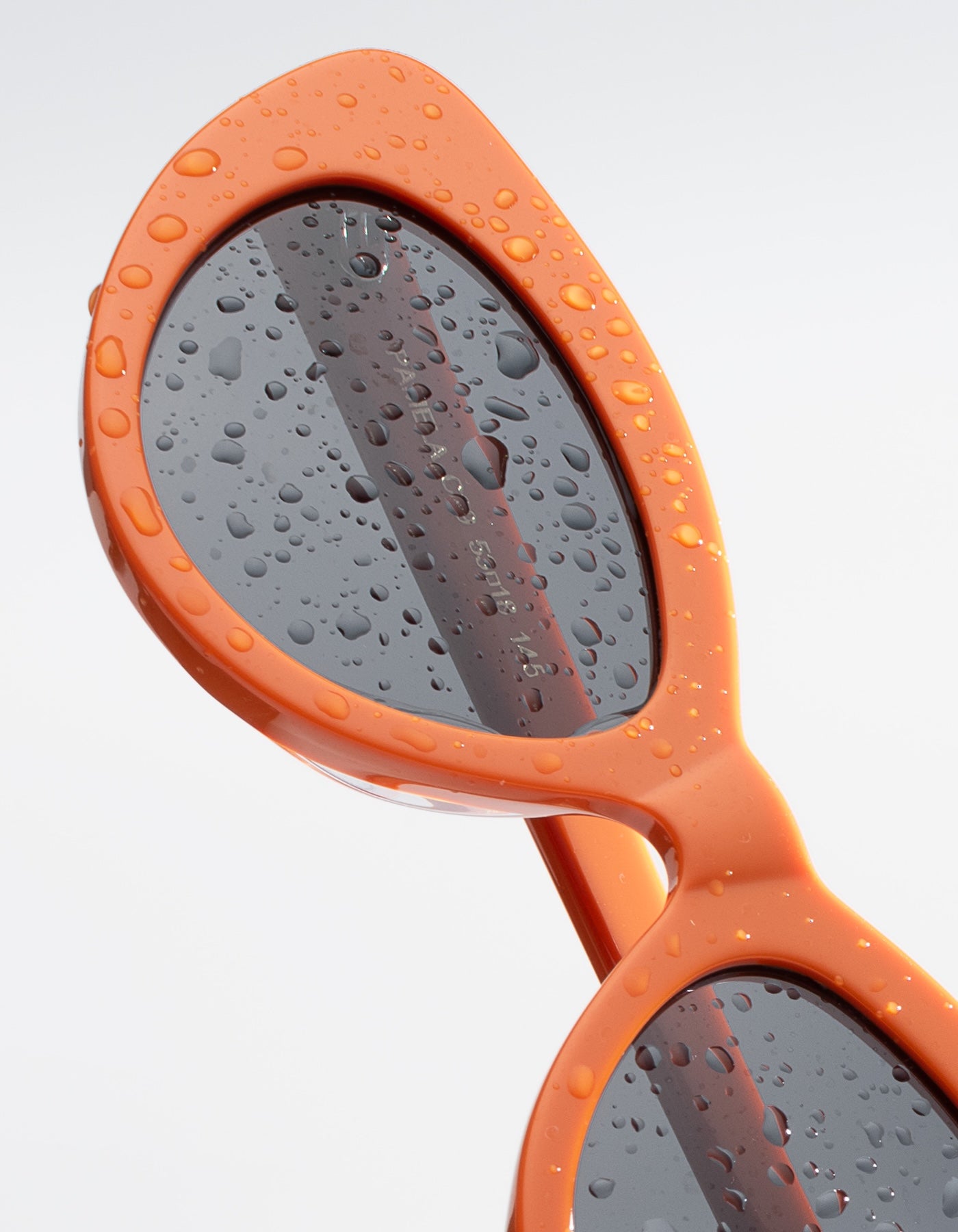 Close up of Pamela Sunglasses in Aperol with water droplets against a light gray background