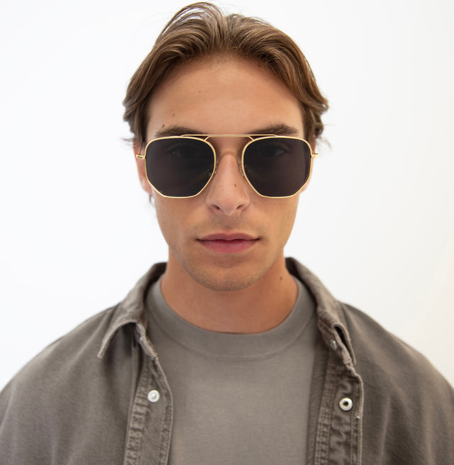 Man with light brown wavy hair wearing Patmos Sunglasses Gold with Grey Flat
