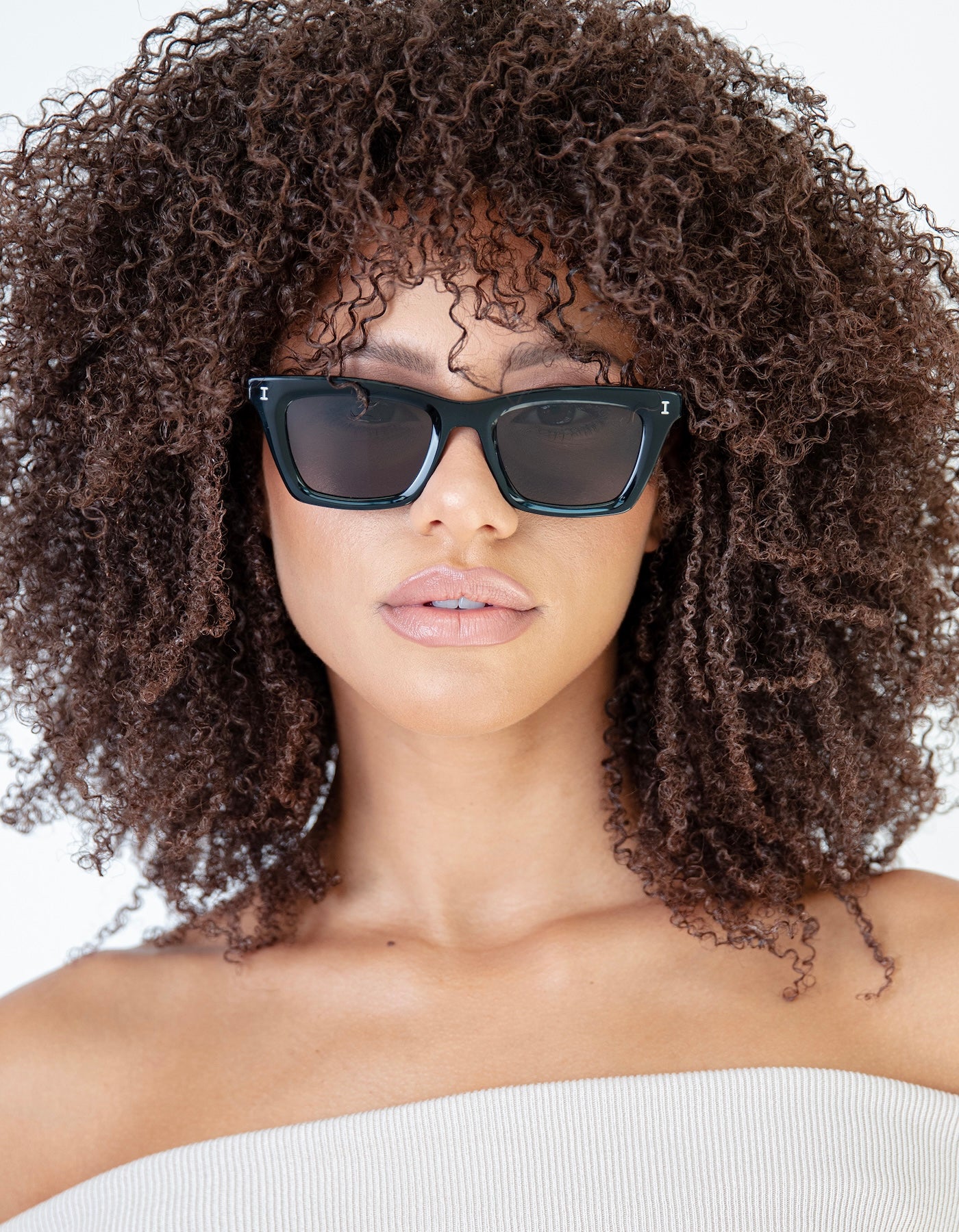 Woman with natural curls in a cream knit tube top wearing the Portugal Sunglasses in Black with Grey lenses