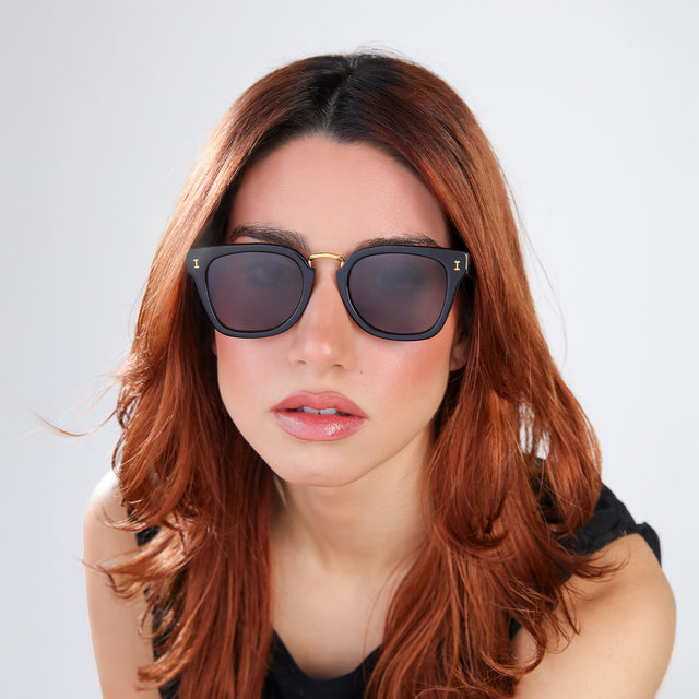 Woman with red hair in a black blouse wearing Positano Sunglasses Black/Gold with Grey