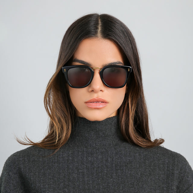 Brunette woman in a gray turtleneck wearing Positano Sunglasses Black/Gold with Grey