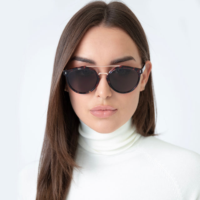 Brunette model with straight hair wearing Puglia Sunglasses Sea Glass/Rose Gold with Grey Flat