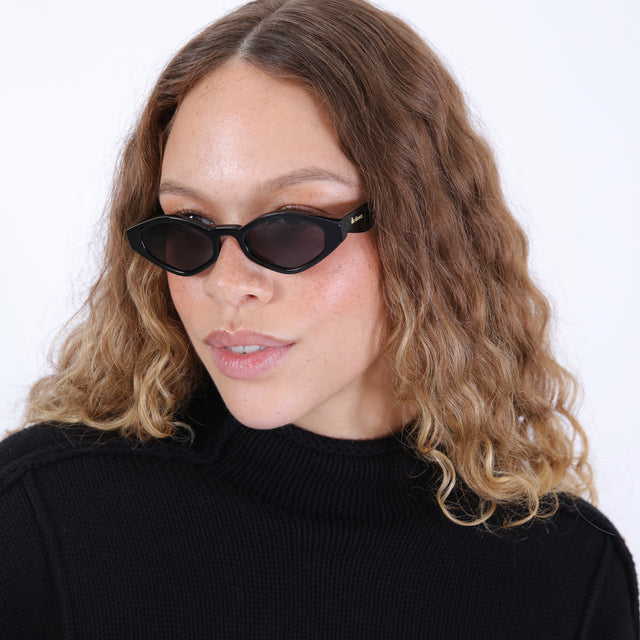 Brunette model with wavy hair in a black sweater wearing Sally Sunglasses Black with Grey