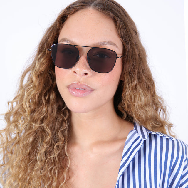 Brunette model with ombré, curly hair wearing Samos Sunglasses Black with Grey Flat