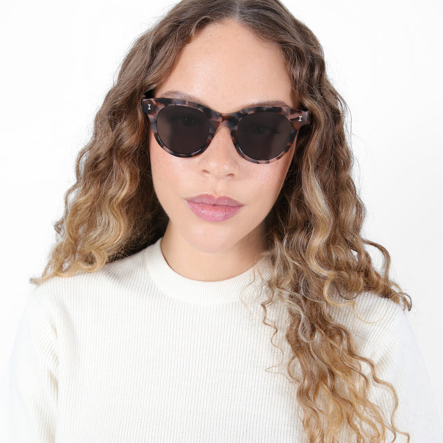 Brunette model with ombré, natural curls wearing Sicilia Sunglasses Blush Tortoise with Grey