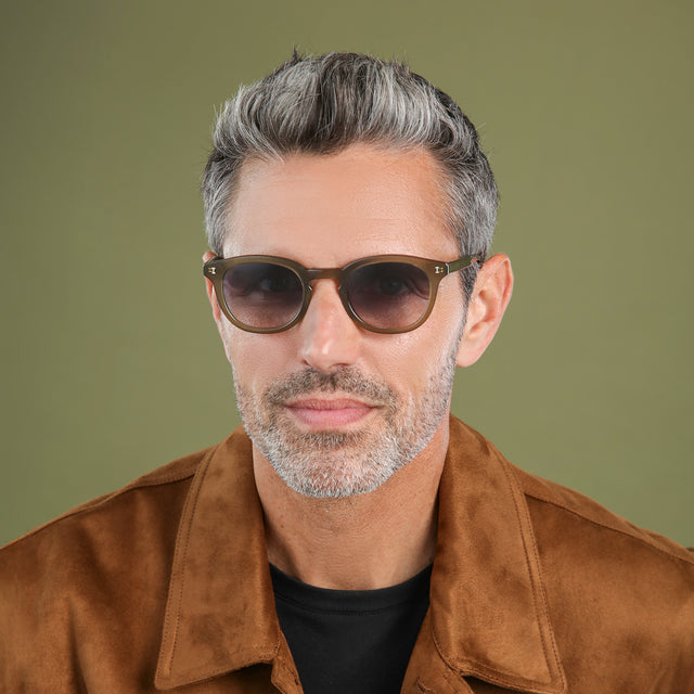 Man with salt and pepper hair and beard in a brown suede jacket wearing Slope Sunglasses Olive with Grey Gradient