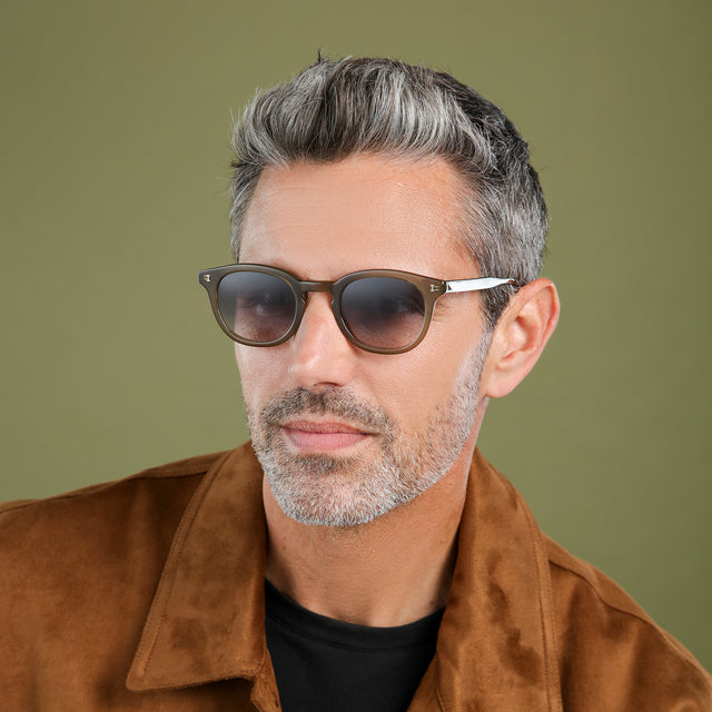 Man in a brown suede jacket looking right wearing Slope Sunglasses Olive with Grey Gradient