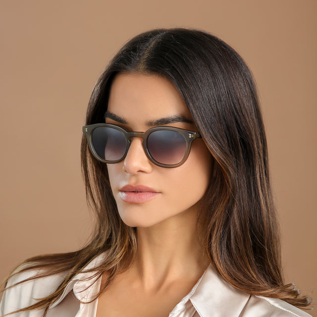 Another angle of brunette woman in a cream silk blouse wearing Slope Sunglasses Olive with Grey Gradient