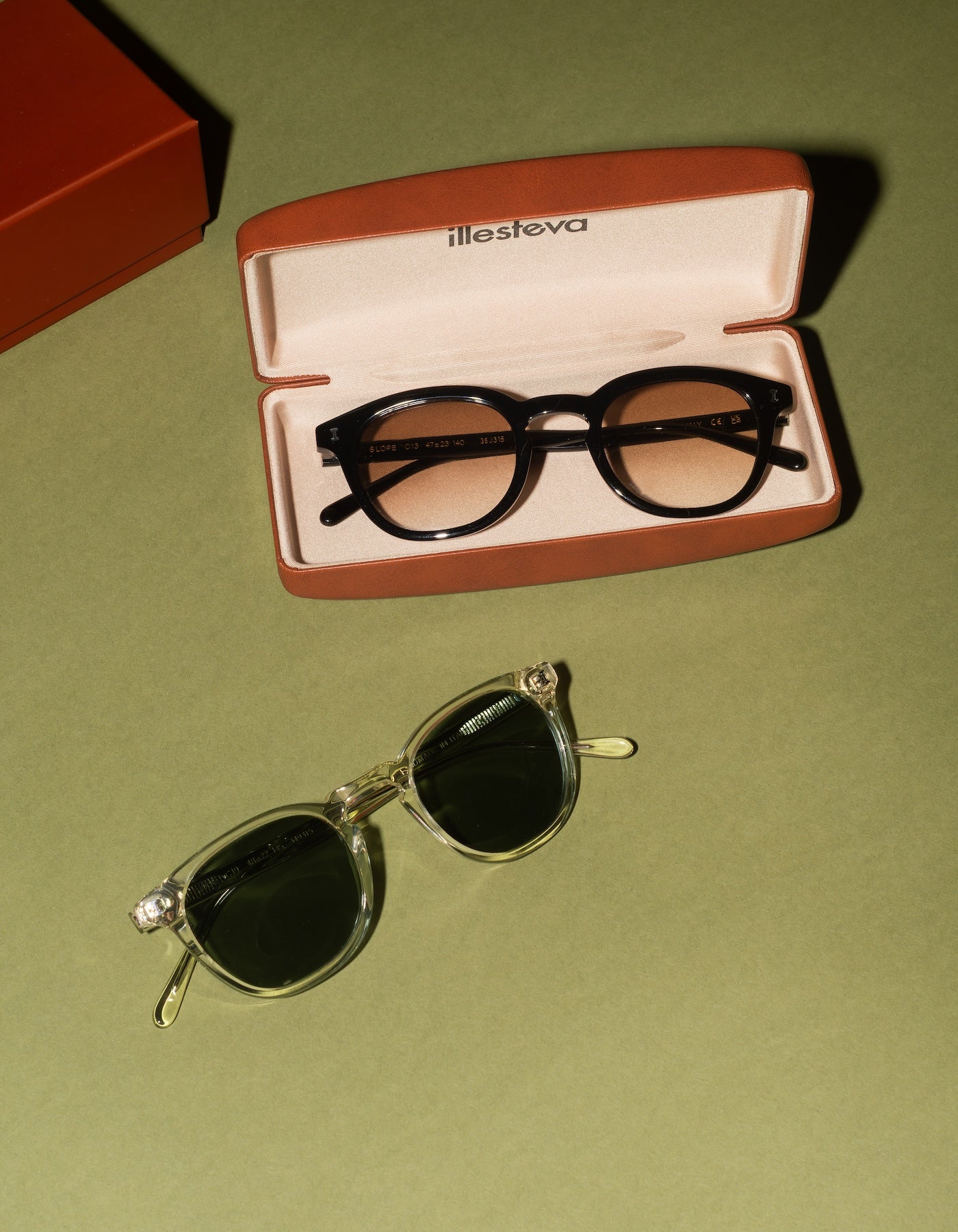 The Slope Sunglasses shown in both Black and Champagne on a green surface