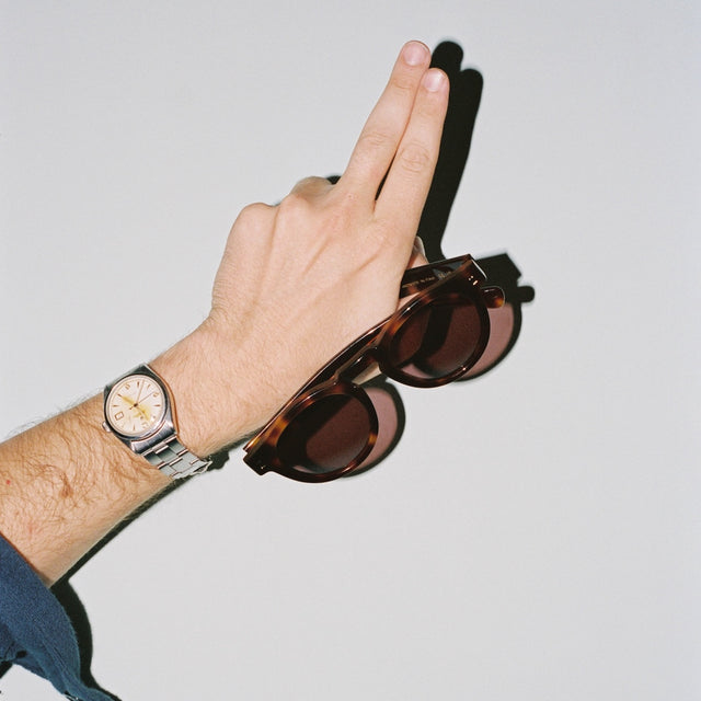 Man with a nice watch holding the collaboration sunglasses  Havana with Plum See Through