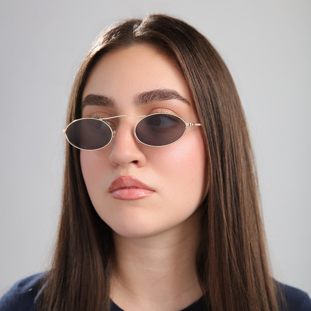 Another angle of brunette model in front of a grey wall wearing Sydney Sunglasses Gold with Grey