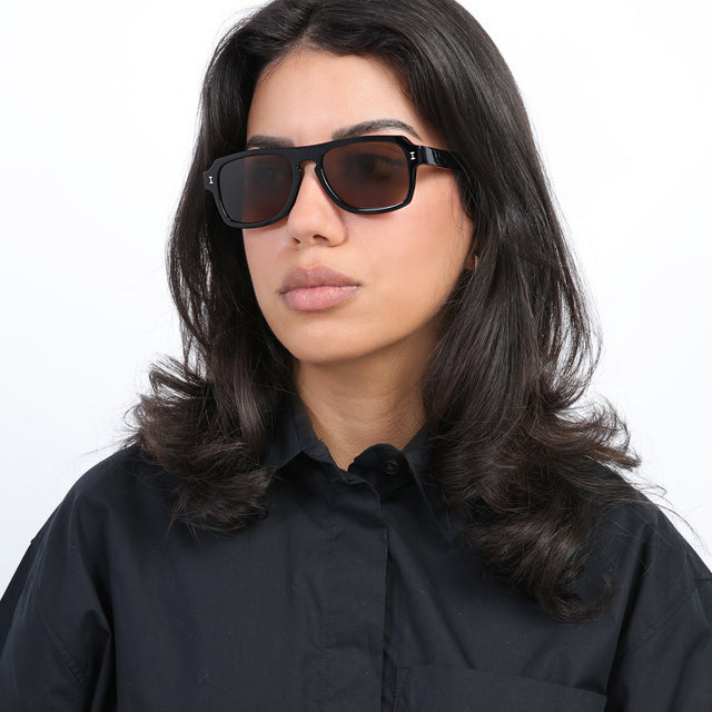 Brunette model with loose curls looking right wearing Trancoso Sunglasses Black with Brown